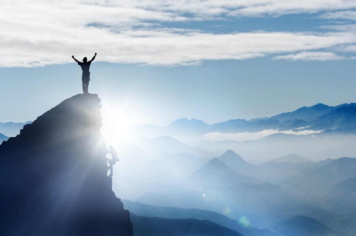 A person standing on the edge of a cliff raising their arms high in the air, ready to take on the world.